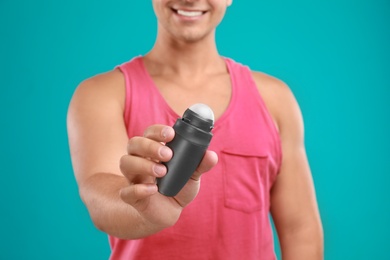 Photo of Young man holding deodorant on blue background, closeup. Mockup for design