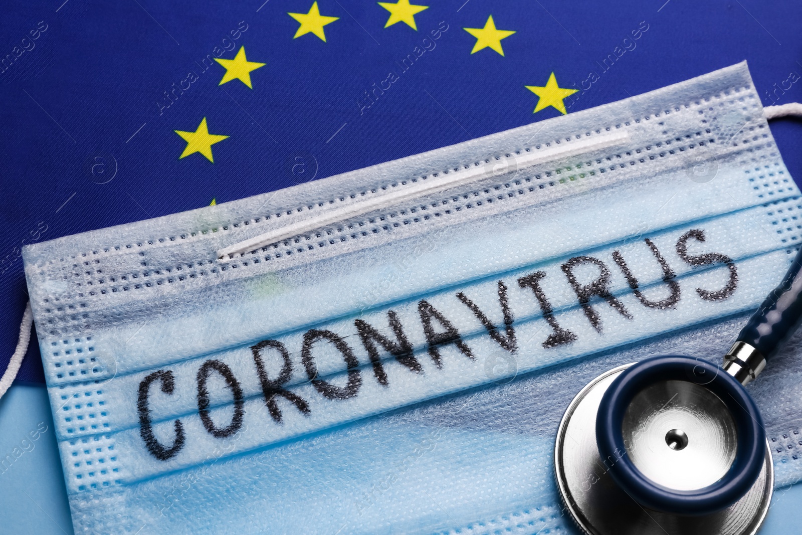 Photo of European Union flag, protective mask and stethoscope on light blue background, closeup. Coronavirus outbreak