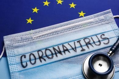 European Union flag, protective mask and stethoscope on light blue background, closeup. Coronavirus outbreak