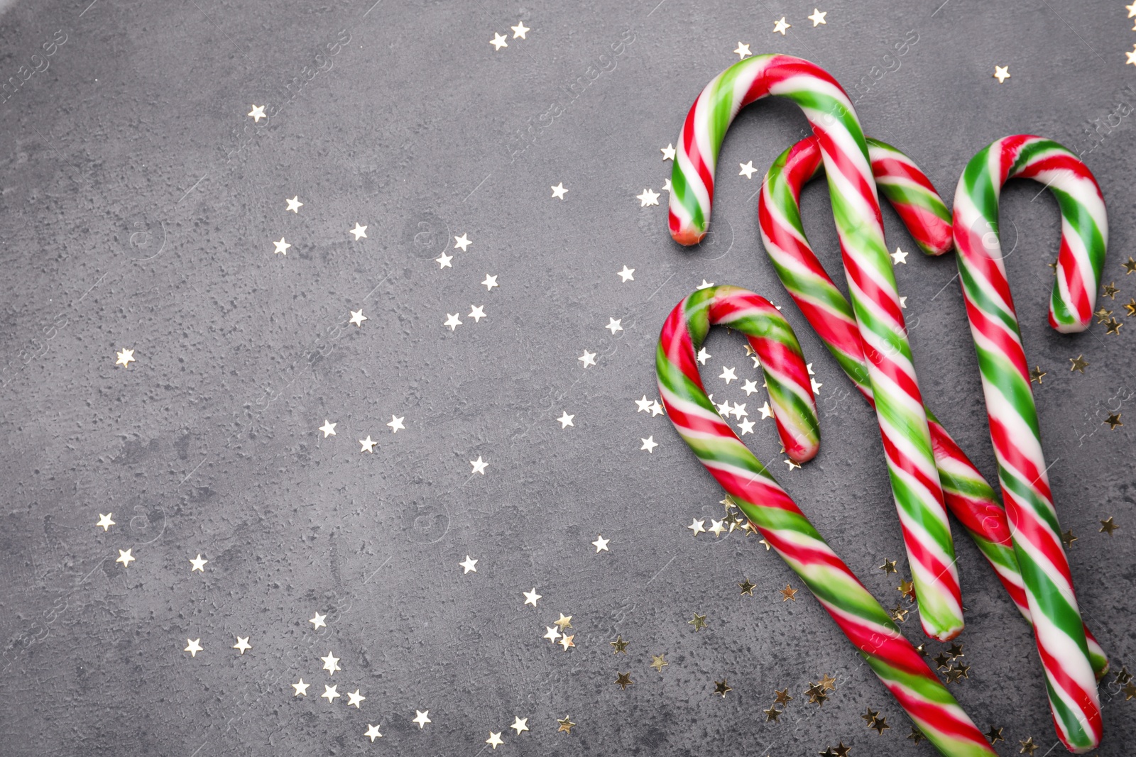 Photo of Many sweet Christmas candy canes and shiny confetti on grey background, flat lay. Space for text