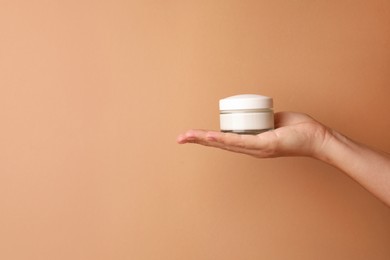 Photo of Woman holding jar of face cream on beige background, closeup. Space for text