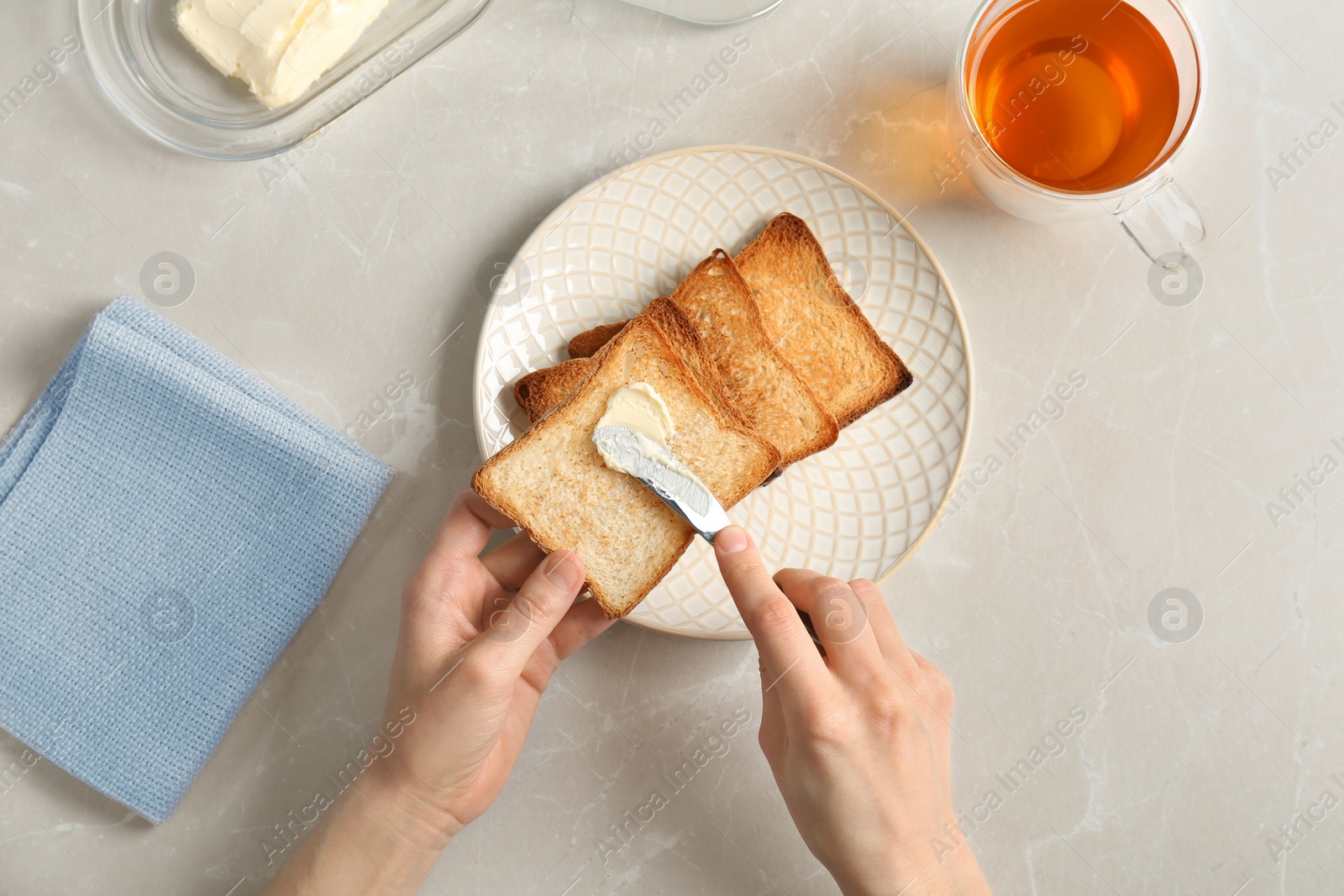 Photo of Woman spreading butter on toasted bread at table, top view