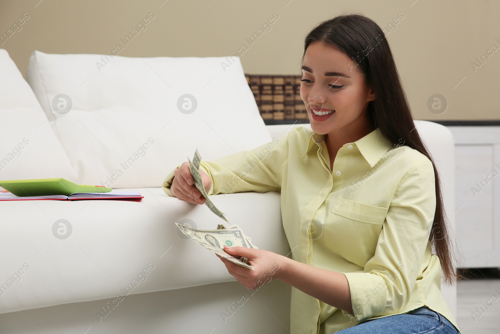 Photo of Young woman counting money near sofa at home