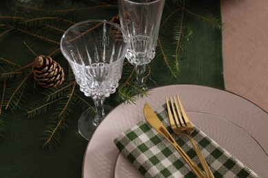 Photo of Christmas place setting with cutlery, glasses and festive decor on table, closeup