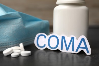 Word Coma with bottle of pills and medical mask on grey table, closeup