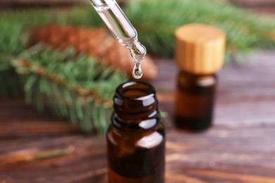 Photo of Dripping pine essential oil into bottle at wooden table, closeup