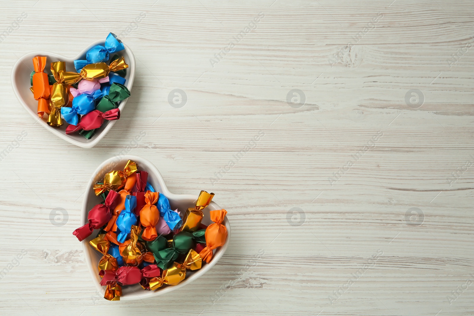 Photo of Candies in colorful wrappers on beige wooden table, flat lay. Space for text