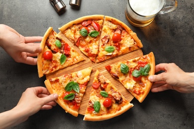 Photo of People taking slices of delicious pizza with tomatoes and sausages at table