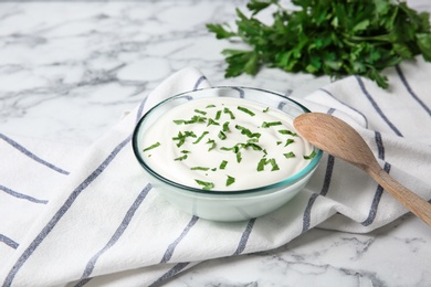 Glass bowl of fresh sour cream with parsley and wooden spoon on marble table