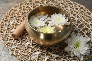 Photo of Tibetan singing bowl with water, beautiful chrysanthemum flowers and mallet on table