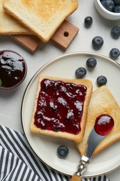 Photo of Toasts served with blueberry jam on light table, flat lay