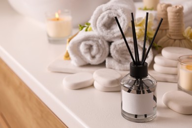Photo of Aromatic reed air freshener and spa stones on white table, space for text