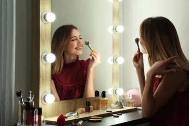 Woman applying makeup near mirror with light bulbs in dressing room