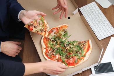 Photo of Office employees having pizza for lunch at workplace, closeup. Food delivery
