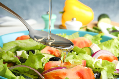 Photo of Adding cooking oil to delicious salad on table, closeup