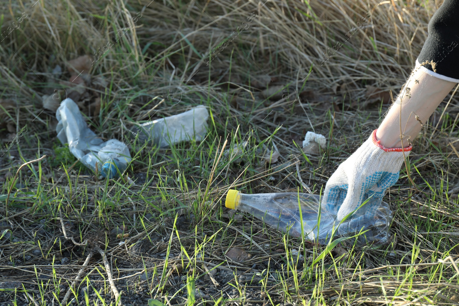 Photo of Woman picking up plastic bottle outdoors, closeup. Space for text