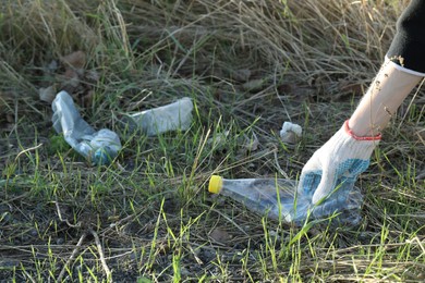 Photo of Woman picking up plastic bottle outdoors, closeup. Space for text