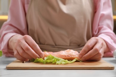 Photo of Woman making delicious spring roll at white table, closeup