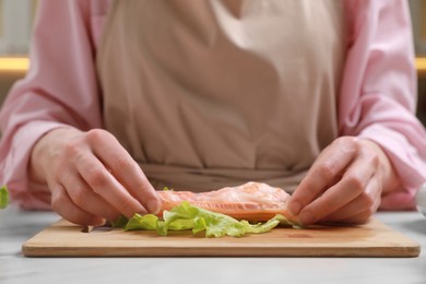 Woman making delicious spring roll at white table, closeup