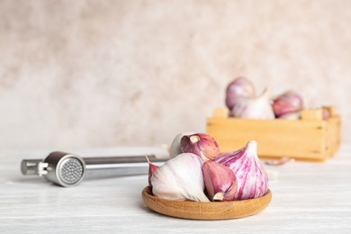 Photo of Garlic press and plate with cloves on table