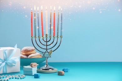 Hanukkah celebration. Menorah with burning candles, dreidels, gift boxes and donuts on light blue table, space for text