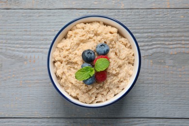 Photo of Tasty oatmeal porridge with berries on grey wooden table, top view