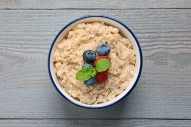 Tasty oatmeal porridge with berries on grey wooden table, top view