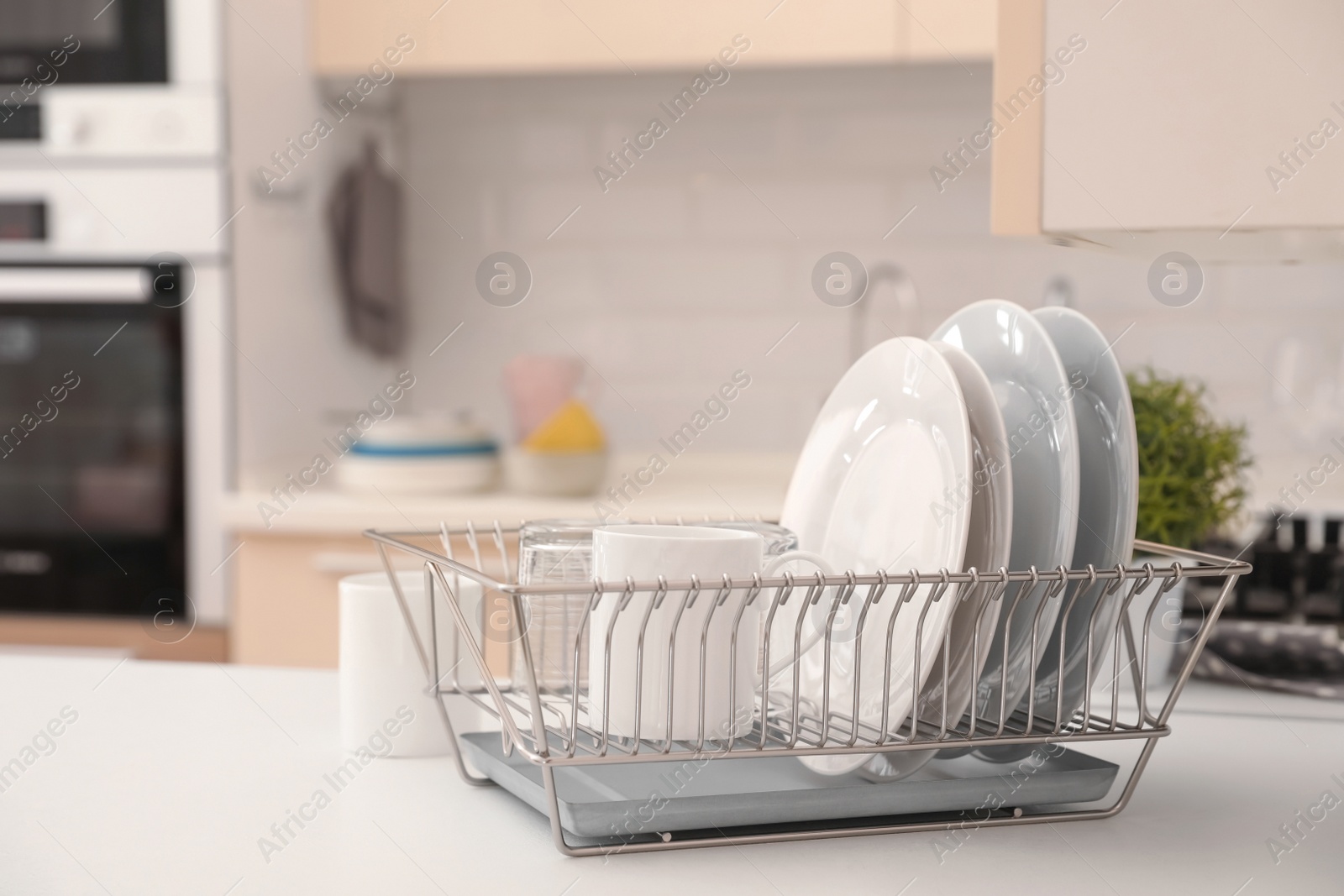 Photo of Dish drainer with clean dinnerware on table in kitchen