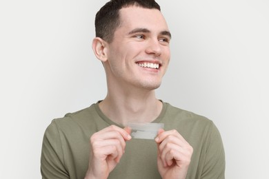 Young man with whitening strips on light grey background