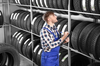 Photo of Young male mechanic with clipboard near tires in automobile service center