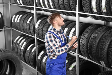 Young male mechanic with clipboard near tires in automobile service center