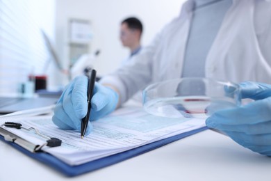 Laboratory worker holding petri dish with blood sample while working at white table, closeup