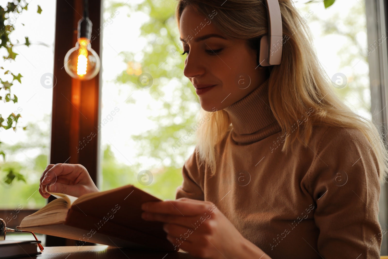 Photo of Woman listening to audiobook at table in cafe, closeup