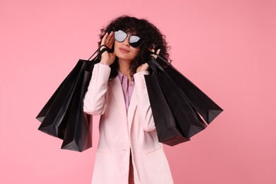 Photo of Happy young woman with shopping bags and stylish sunglasses on pink background