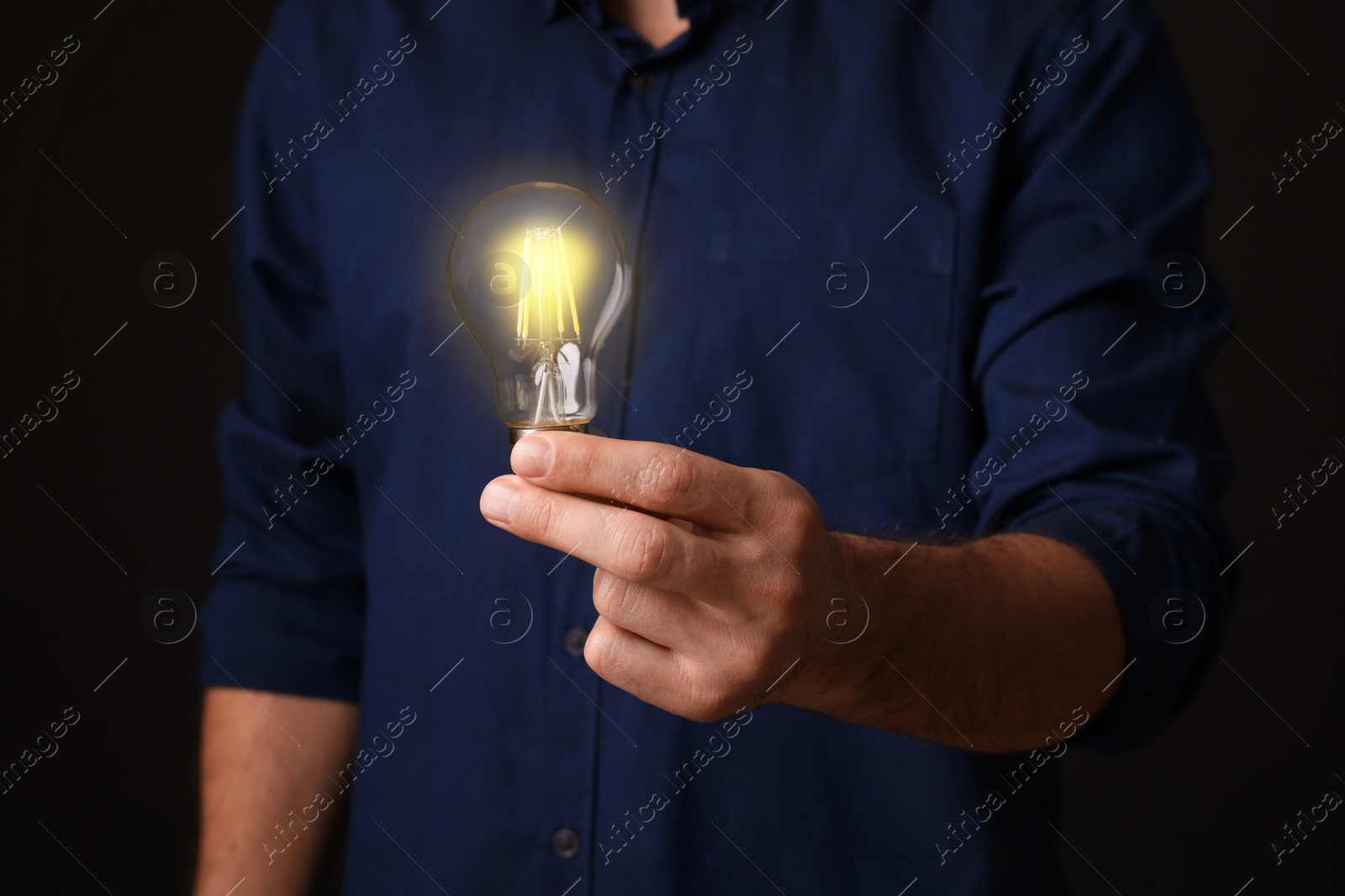 Photo of Glow up your ideas. Closeup view of man holding light bulb on black background