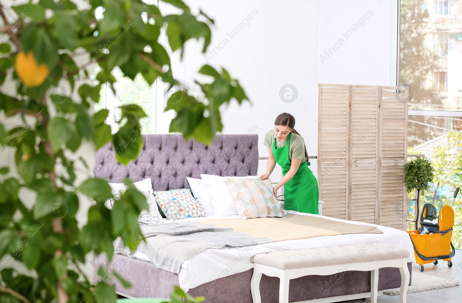 Photo of Worker of cleaning service making bed in room