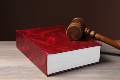 Law. Book and gavel on wooden table against brown background, closeup