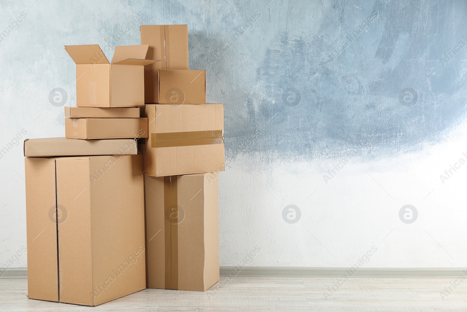 Photo of Pile of cardboard boxes near color wall indoors. Space for text