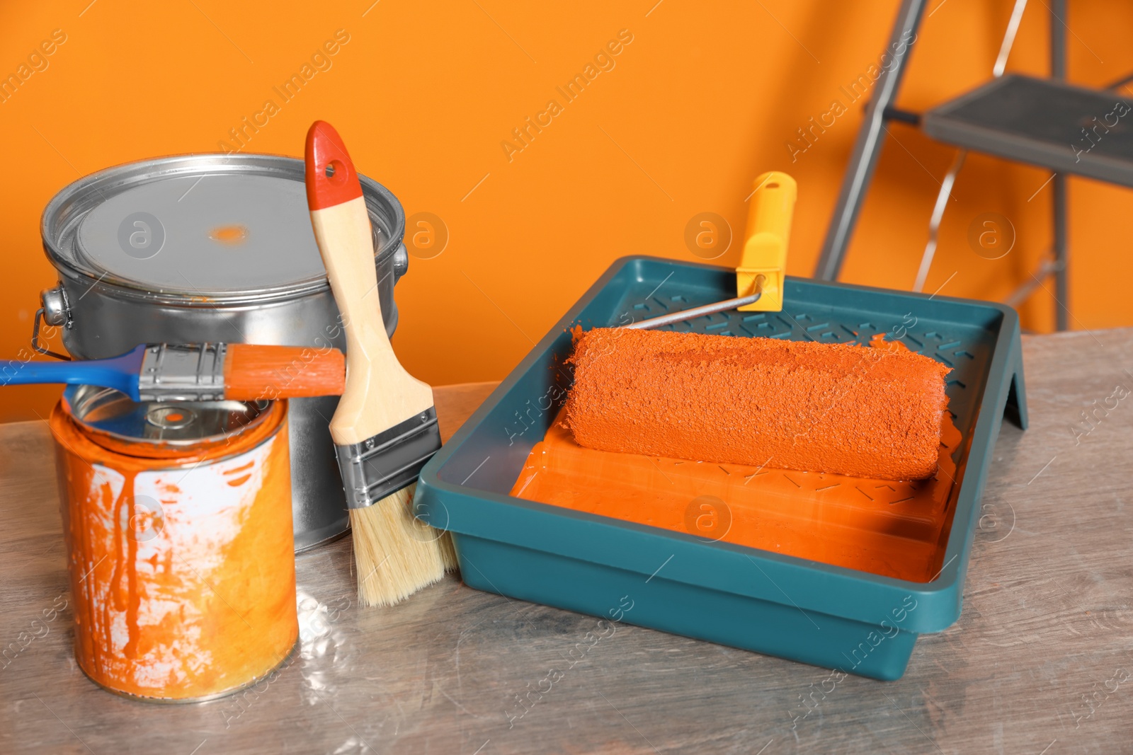 Photo of Tray with orange paint and roller on table