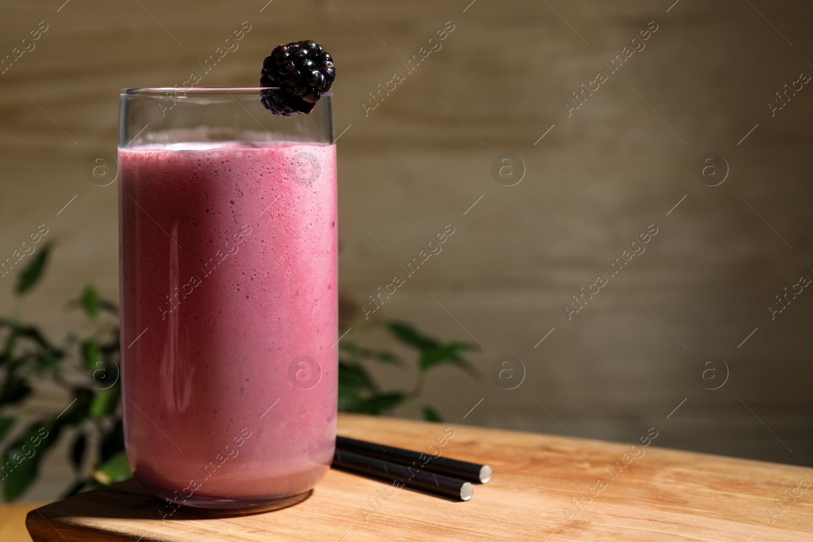 Photo of Glass of blackberry smoothie on wooden table. Space for text