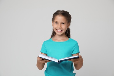 Photo of Portrait of cute little girl reading book on grey background