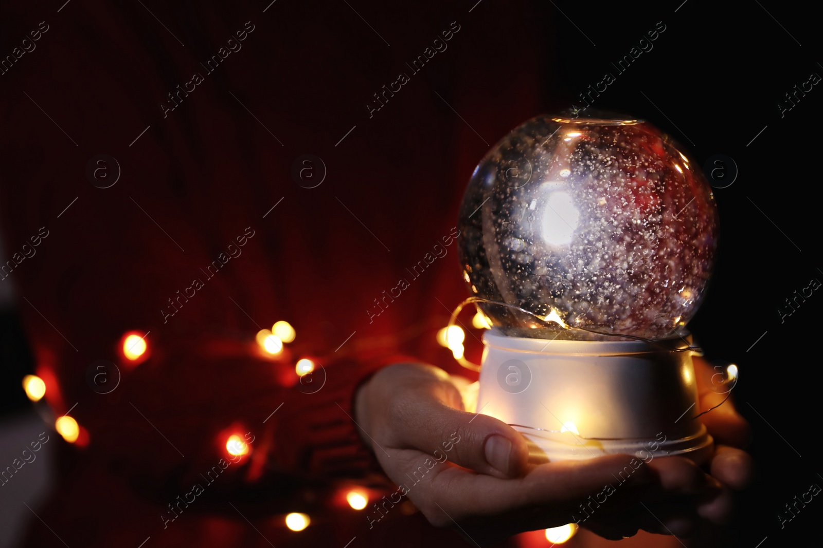 Photo of Woman holding snow globe and Christmas lights, closeup