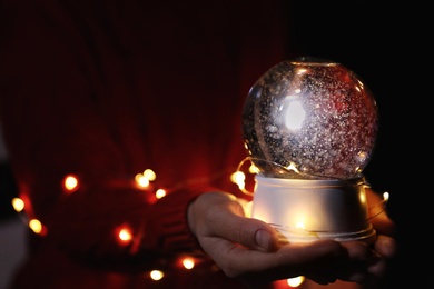 Photo of Woman holding snow globe and Christmas lights, closeup