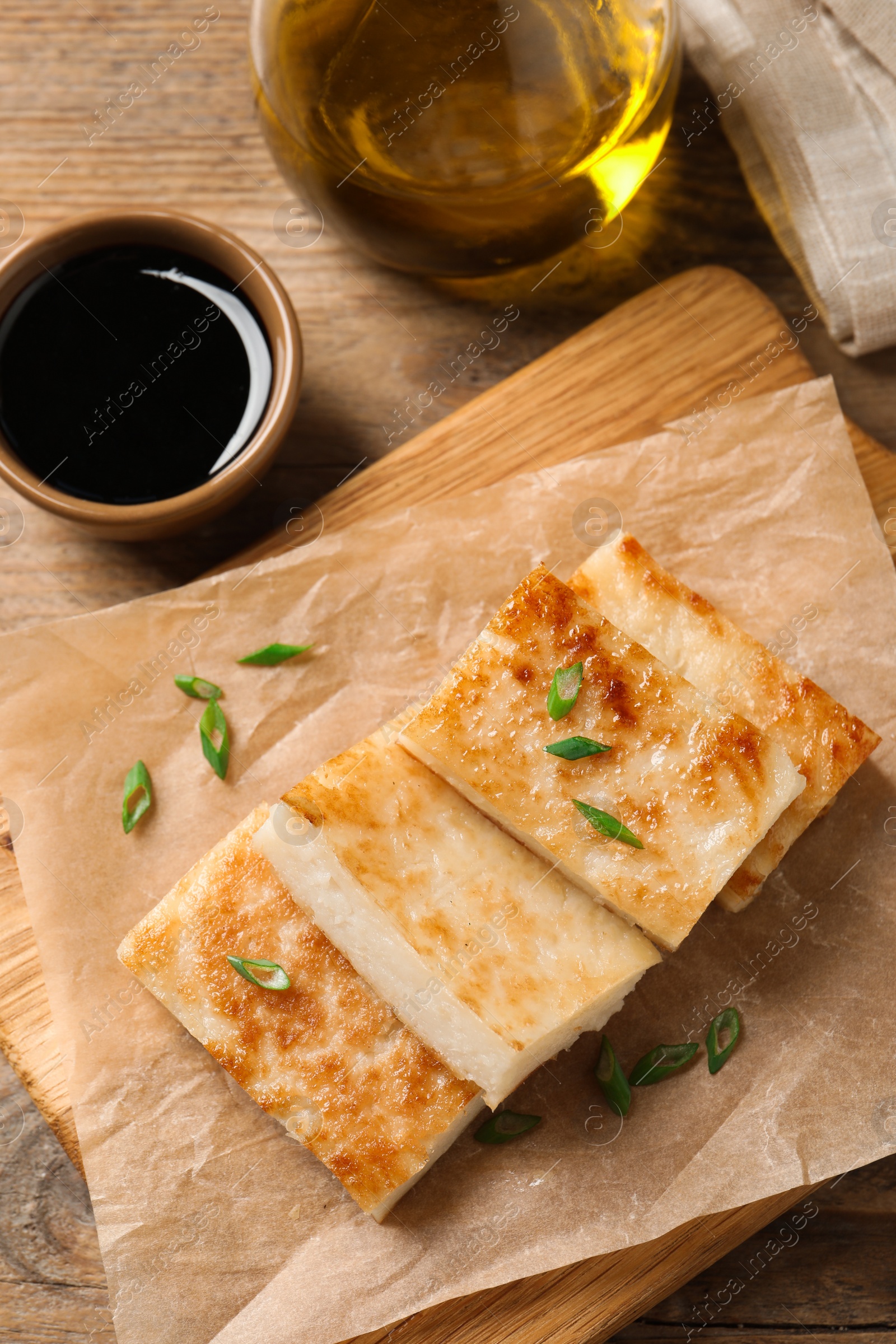 Photo of Delicious turnip cake with green onion and soy sauce on wooden table, flat lay