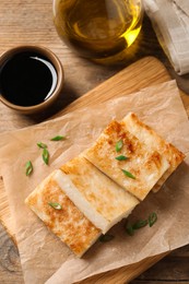 Photo of Delicious turnip cake with green onion and soy sauce on wooden table, flat lay