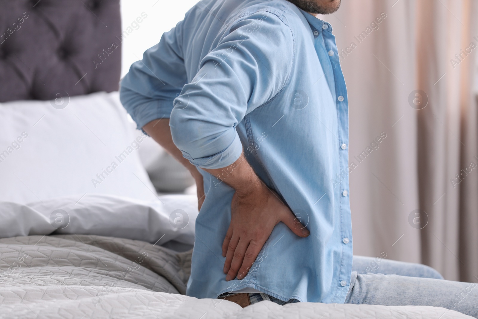 Photo of Young man suffering from back pain at home, closeup