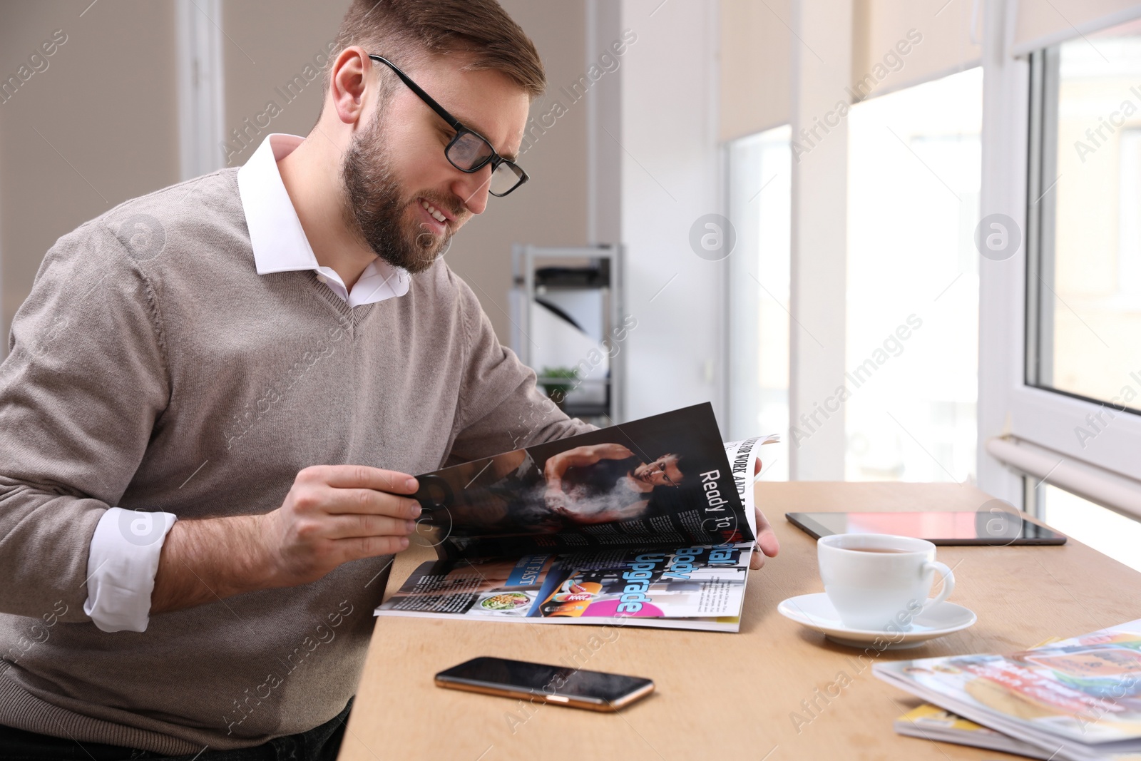 Photo of Young man reading sports magazine at table indoors