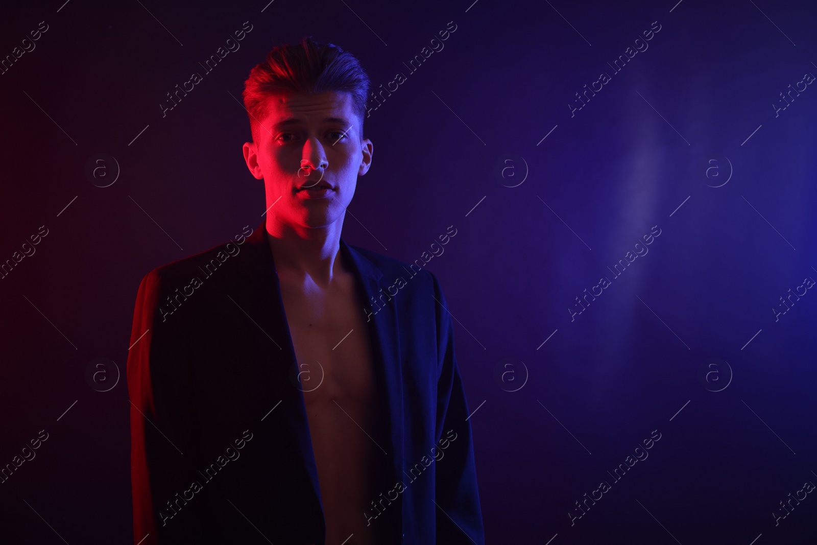 Photo of Sexy young man on dark background in neon lights. Space for text