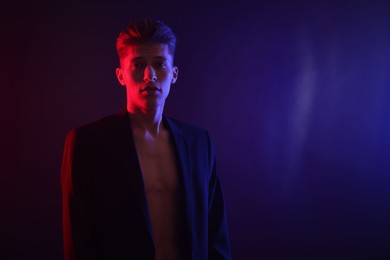 Sexy young man on dark background in neon lights. Space for text