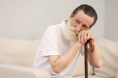 Photo of Senior man with walking cane on sofa indoors